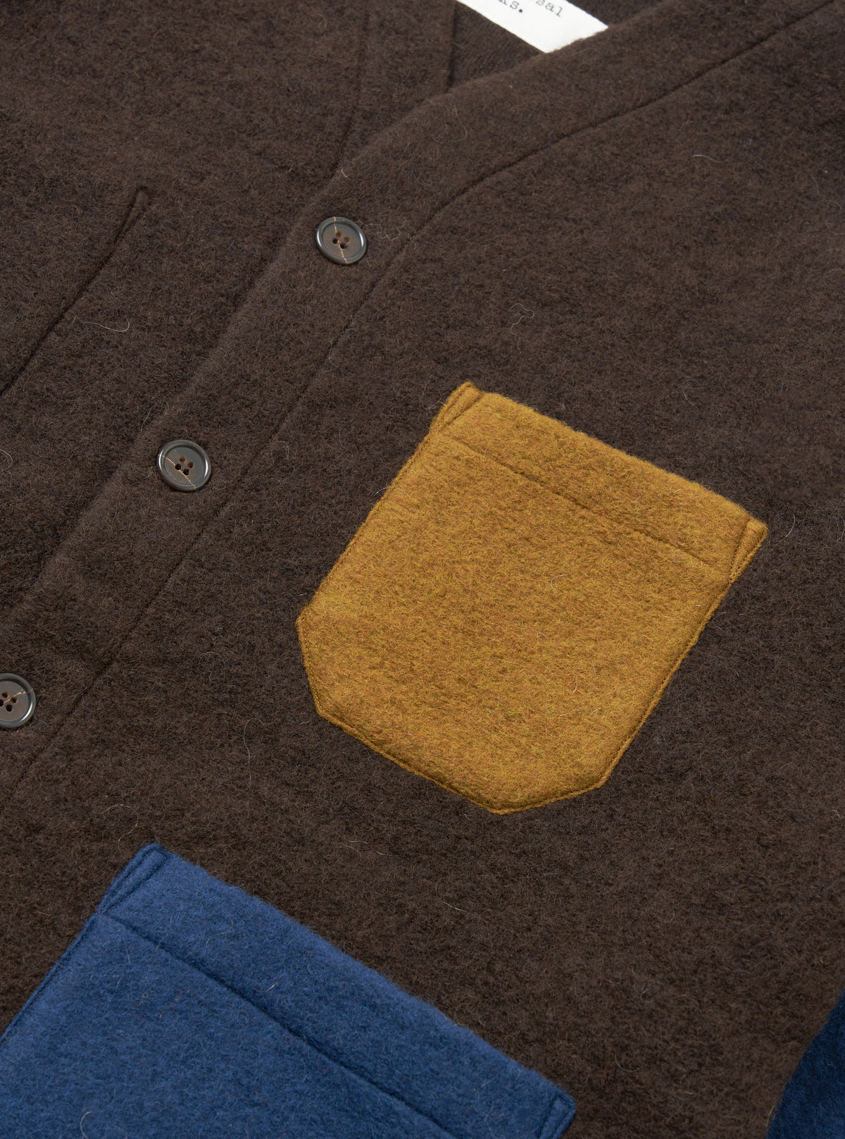 A detailed close-up shot of a model wearing the Brown/Indigo Wool Fleece Cardigan against a plain backdrop, showing the front button details, neat edge binding, patch pocket, and heathered brown-indigo material.