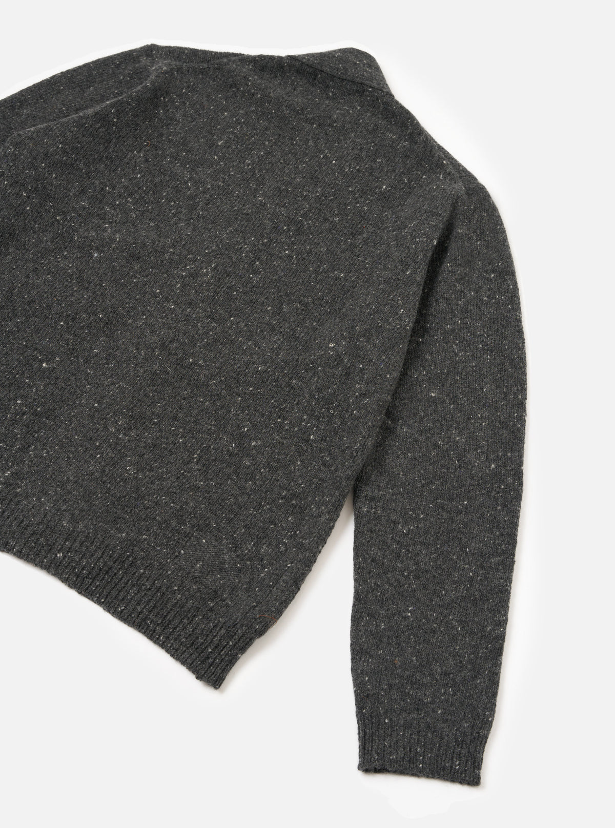 A male model viewed from the rear wearing the Black Wool Fleck Langdale Cardigan against a plain white studio backdrop, highlighting the loose fit silhouette and textured black yarn with subtle flecked detail.