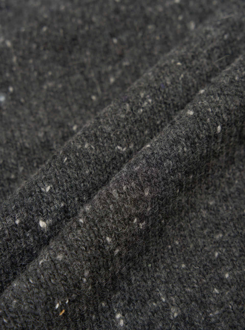 A fabric swatch close-up image of the Black Wool Fleck Langdale Cardigan on a plain light background, highlighting the rich black wool blend base adorned with characteristic subtle multi-colored flecks.