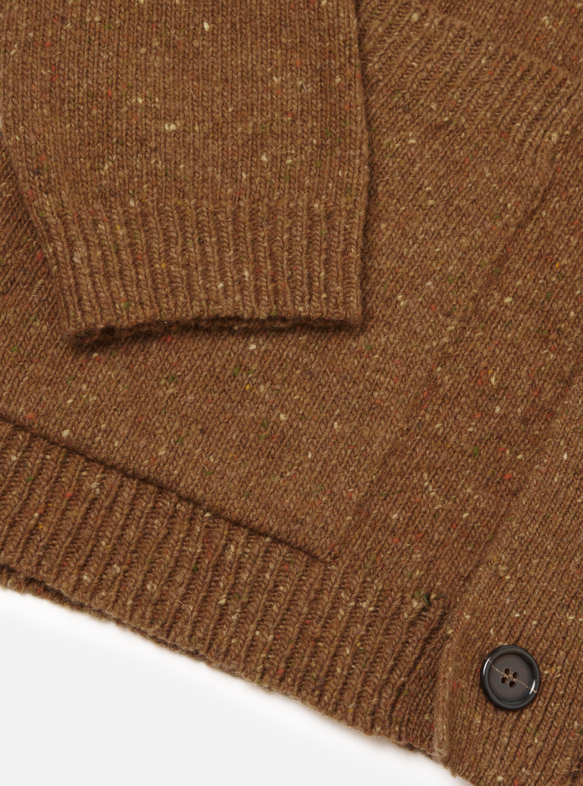 A close-up image of a model wearing the Brown Wool Fleck Langdale Cardigan against a plain backdrop, focusing on the buttoned front, front patch pocket, V-neck collar, and detailed speckle pattern in the yarn.