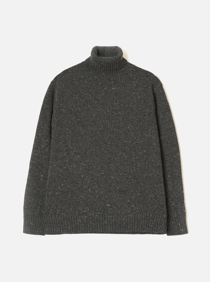 A model wearing the Black Wool Fleck Roll Neck against a neutral studio background. The knitwear piece features a cozy high roll neck, ribbed trim details, and a subtle flecked texture across the recycled wool fabric.