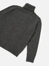 A side view of a model wearing the Black Wool Fleck Roll Neck on a plain background, highlighting the relaxed fit, ribbed cuffs, and soft recycled wool texture with subtle contrasting flecked detailing.