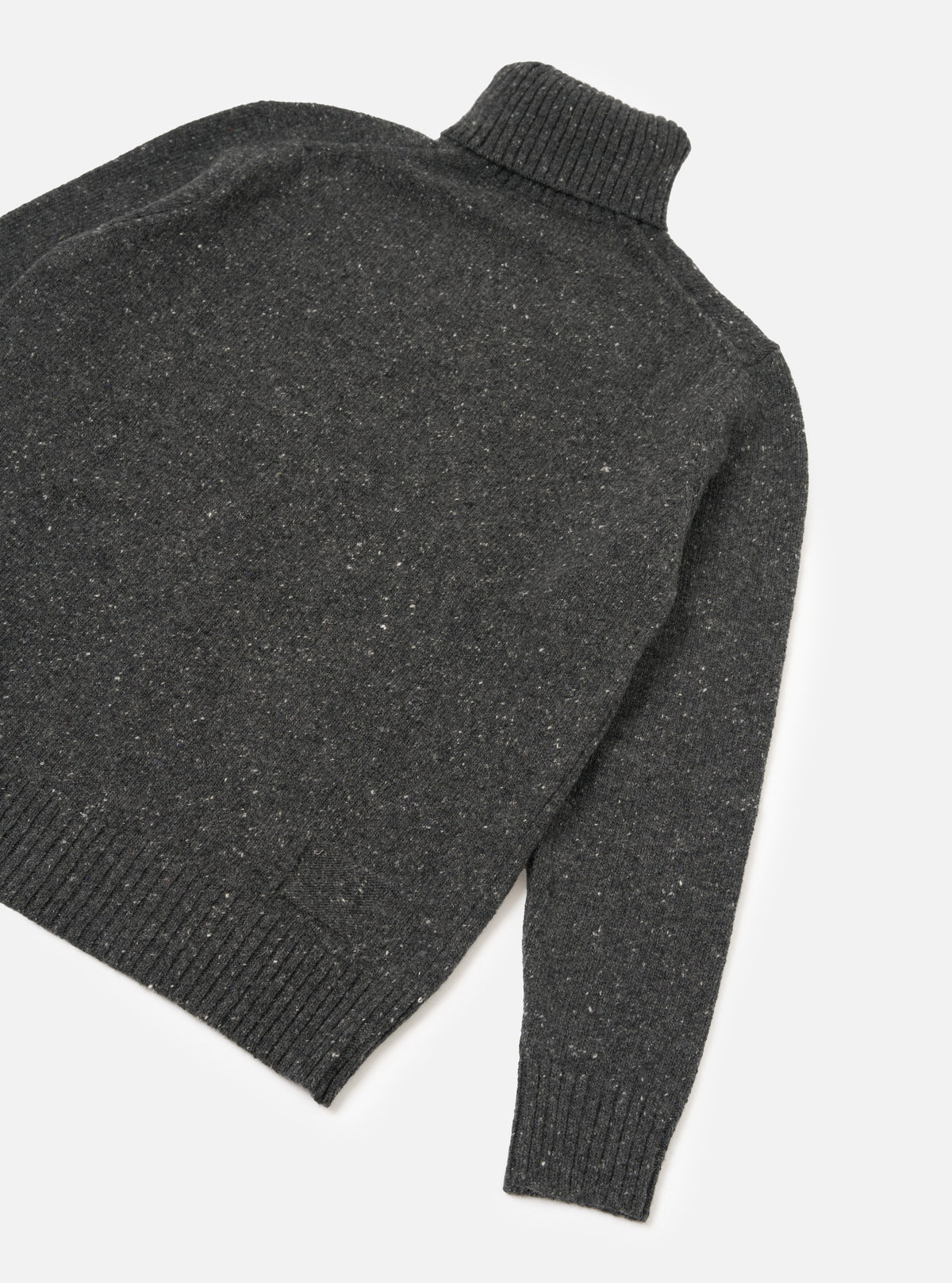 A side view of a model wearing the Black Wool Fleck Roll Neck on a plain background, highlighting the relaxed fit, ribbed cuffs, and soft recycled wool texture with subtle contrasting flecked detailing.