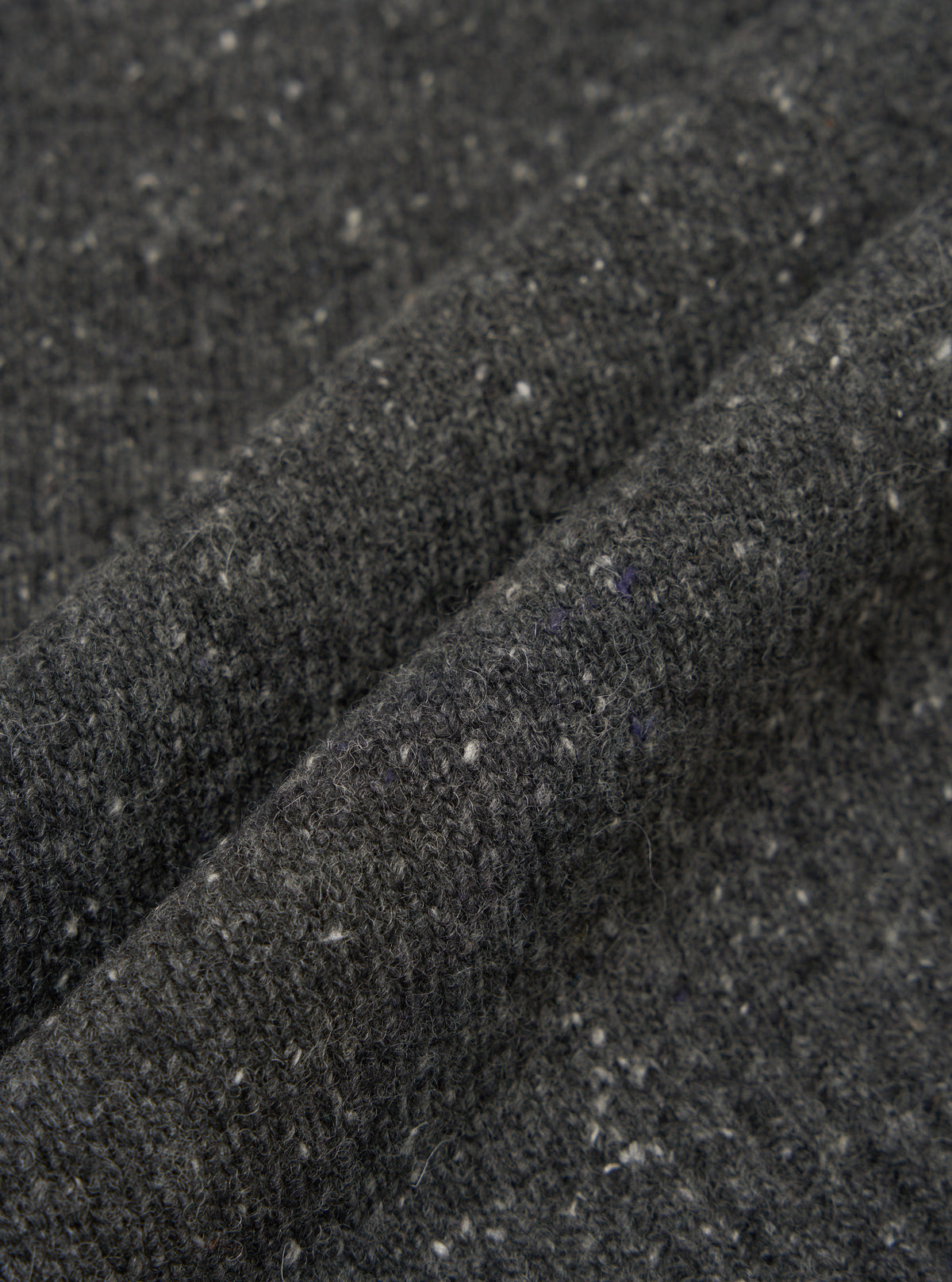 A close-up fabric swatch view of the Black Wool Fleck Roll Neck on a light backdrop, emphasizing the rich black recycled wool material integrated with subtle flecked texture details throughout.