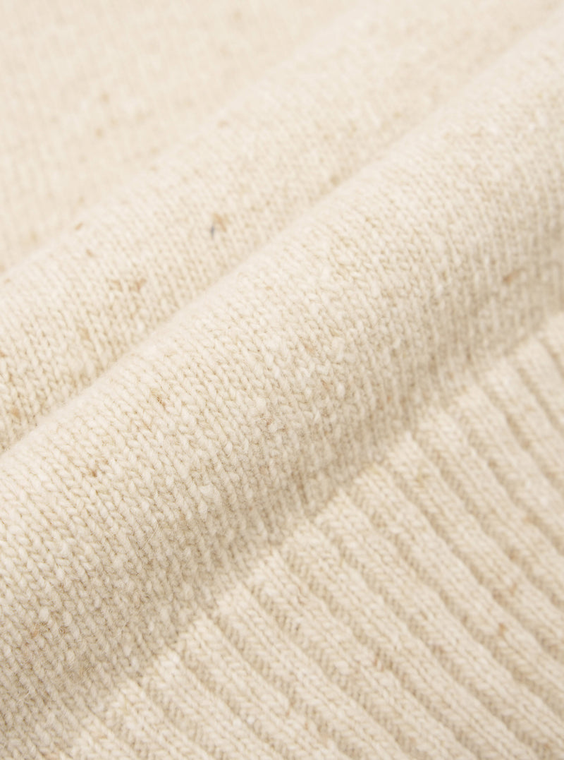 A close-up swatch image of the Fawn Wool Fleck Roll Neck fabric, detailing the soft tactile finish, warm fawn color shade, and delicate flecked recycled wool knit pattern on a plain neutral ground.