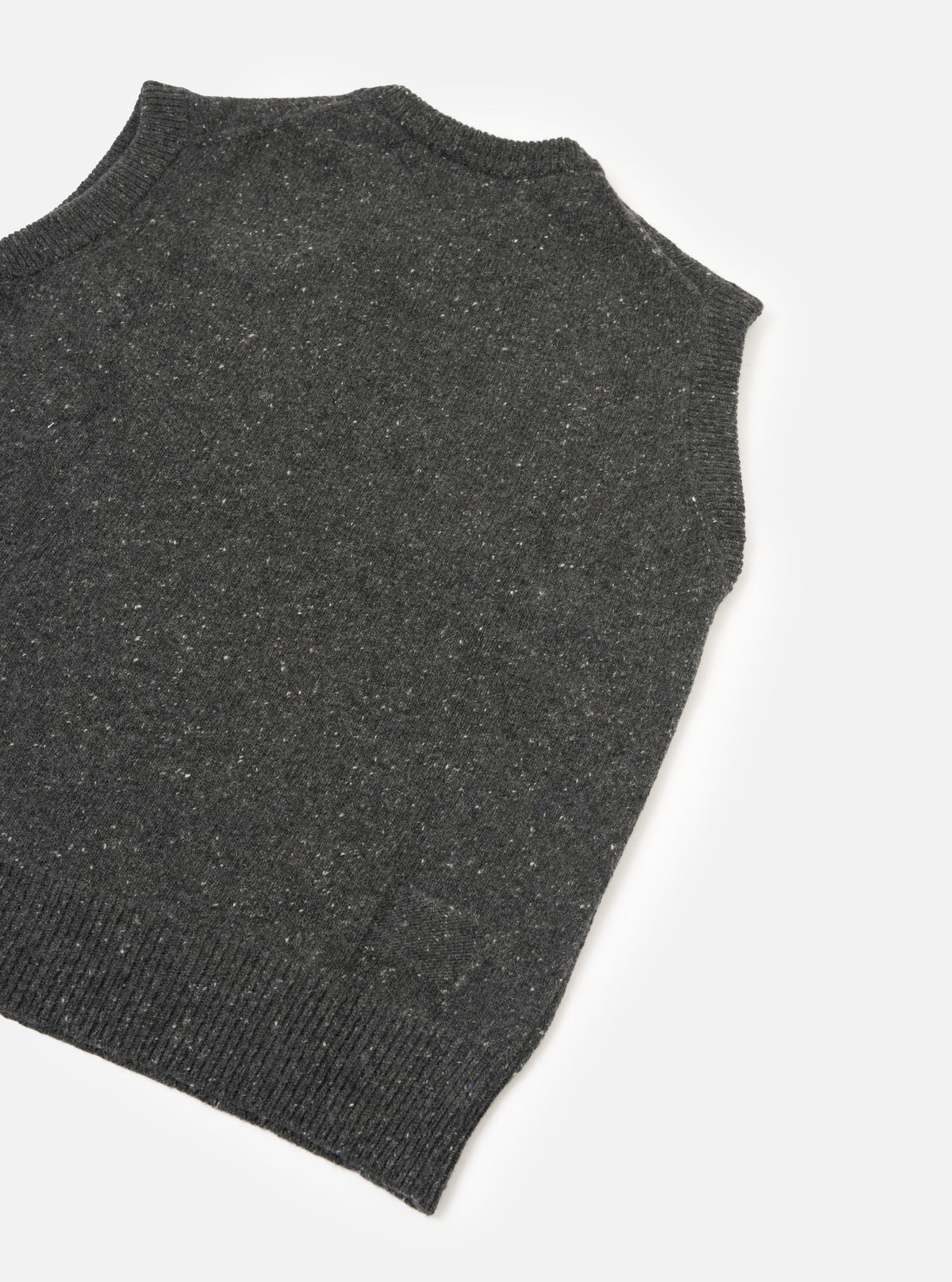 A side profile view of a model wearing the Black Wool Fleck Sweater Vest on a plain background, highlighting the sleeveless cut, neat armhole finishing, and textured dark fleece-flecked knit.
