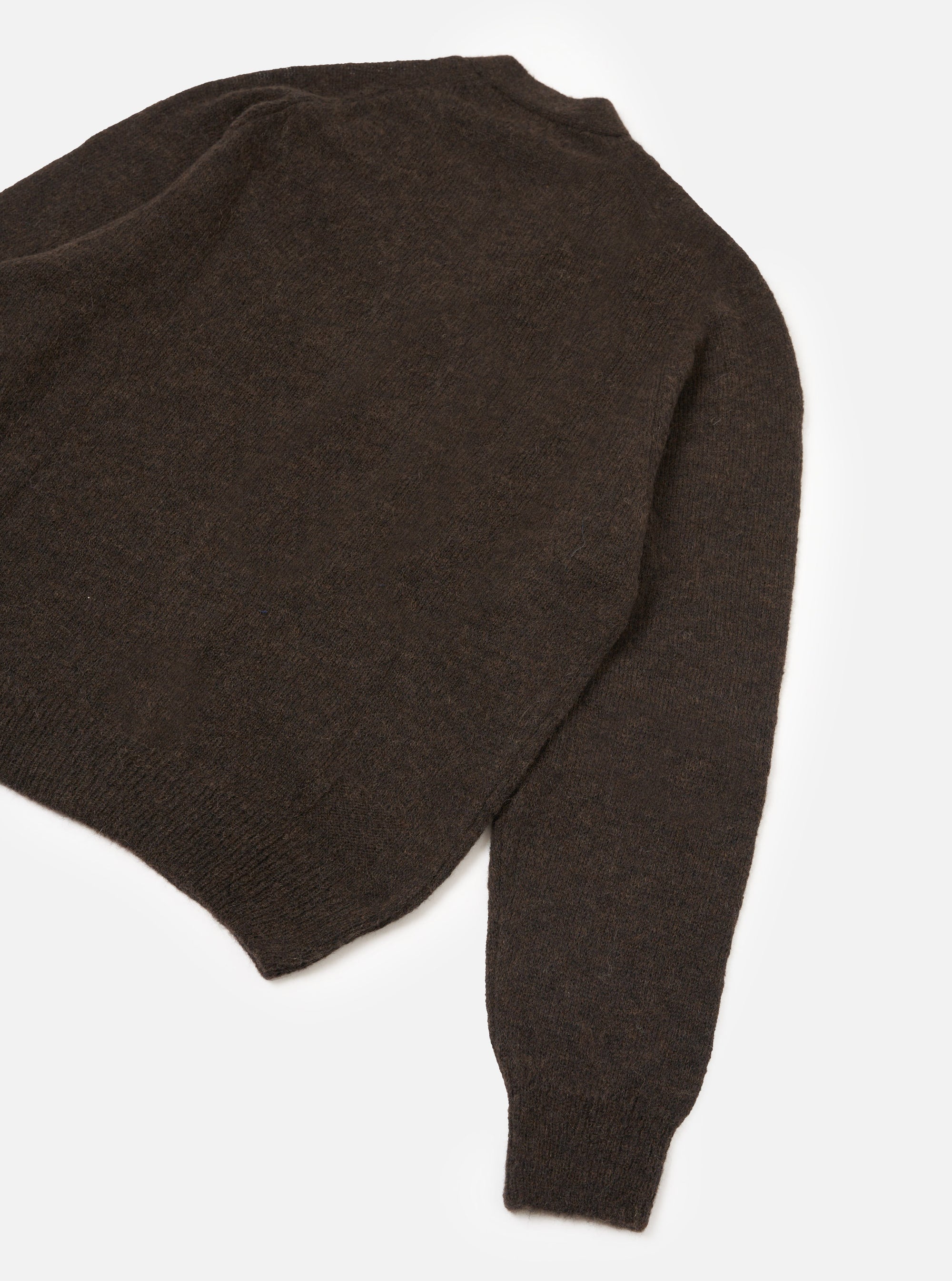 Dark brown alpaca knit cardigan laid flat on a white studio surface, shot from above at an angle. The body, one sleeve, ribbed hem, and ribbed cuff are visible. The fabric has a soft, slightly fluffy texture with a fine, plain knit construction.