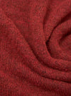 Close-up of the deep orange alpaca knit fabric of the Lyon Crew, showing a soft, fluffy texture with a fine marl knit construction. Dark flecks run throughout the warm red-orange yarn. The fabric is gathered into soft folds, highlighting its weight and drape.