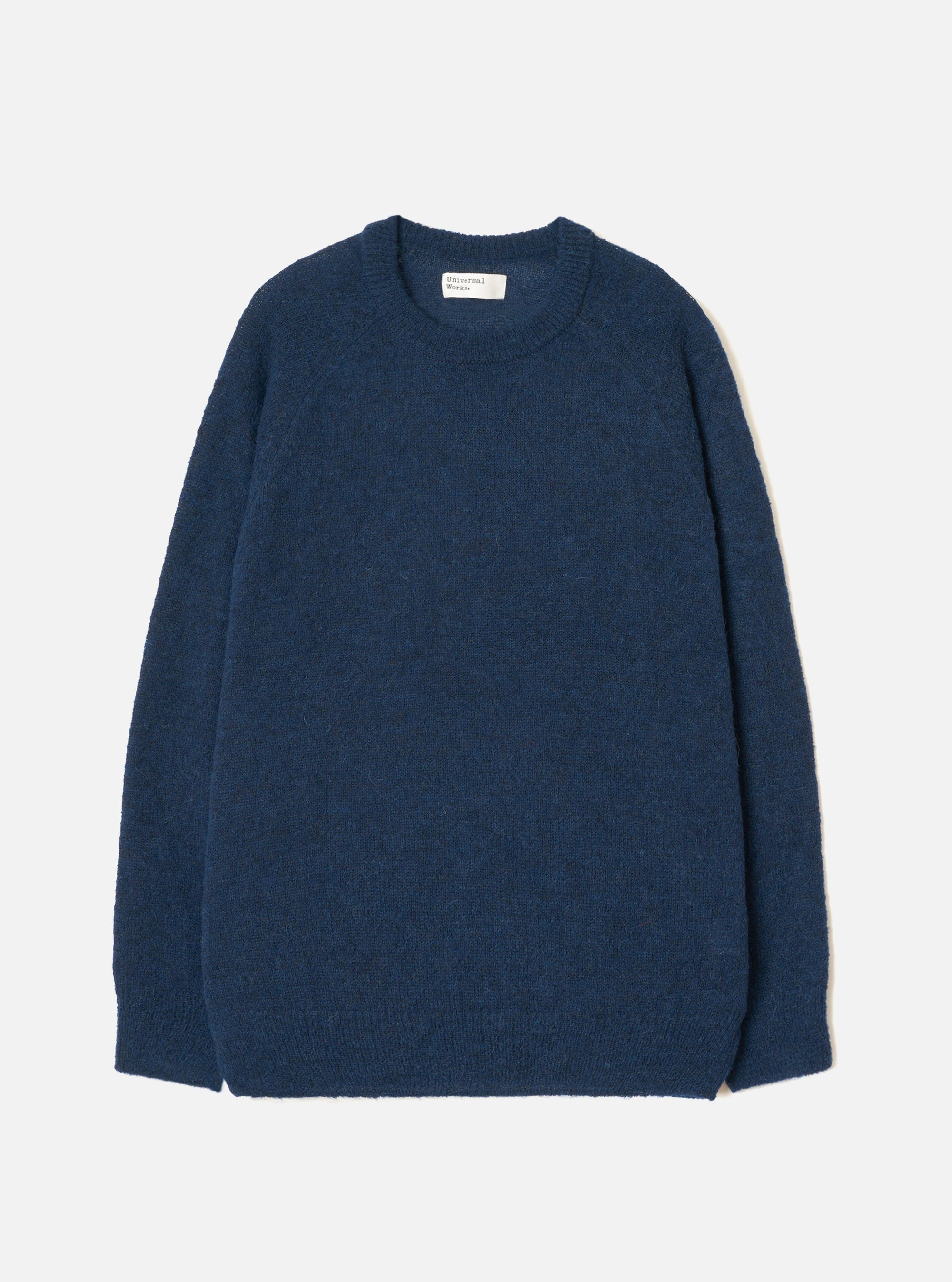 Navy alpaca knit crewneck jumper laid flat on a light grey background. The ribbed crew collar, cuffs and hem contrast with the brushed, fluffy texture of the body and sleeves. A Universal Works woven label sits inside the back neck. Plain navy throughout with no pattern.