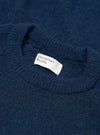Close-up flat lay of the crew neck collar on a navy alpaca knit jumper. The ribbed neckline has a soft, fluffy texture. A white woven Universal Works label is visible inside the collar. The fabric shows a marl-flecked deep navy tone throughout.