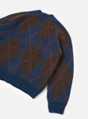 A model wearing the Navy Alpaca Argyle David Cardigan shown from a side angle on a plain background, focusing on the traditional argyle pattern, soft fluffy alpaca fabric, and neat button-front detail.