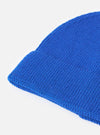An angled view of the Blue Merino Knit Watch Cap on a plain neutral background, highlighting the full shape of the ribbed beanie, pinched crown construction, and rolled cuff detail in vibrant blue.