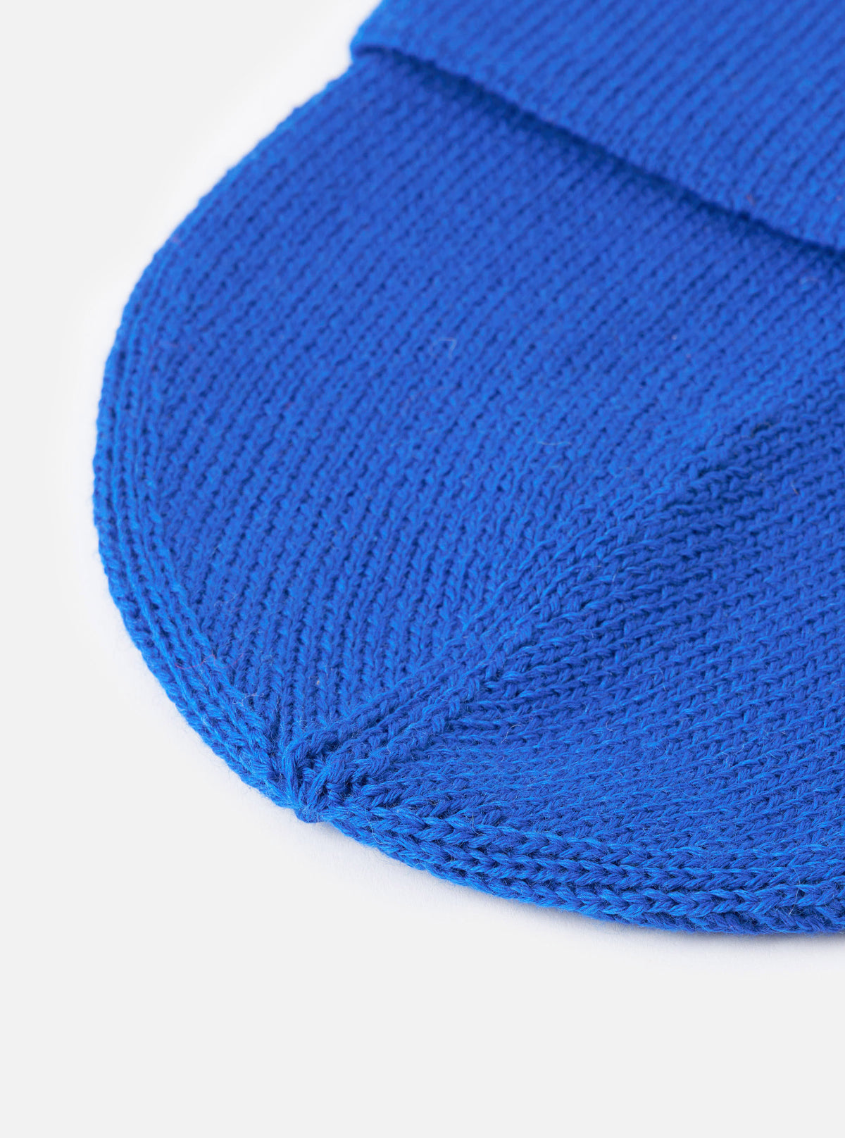 A close-up view of the Blue Merino Knit Watch Cap set against a plain background, focusing on the detailed ribbed knit construction, soft merino wool fibers, and neat finished edging of the turn-up cuff.