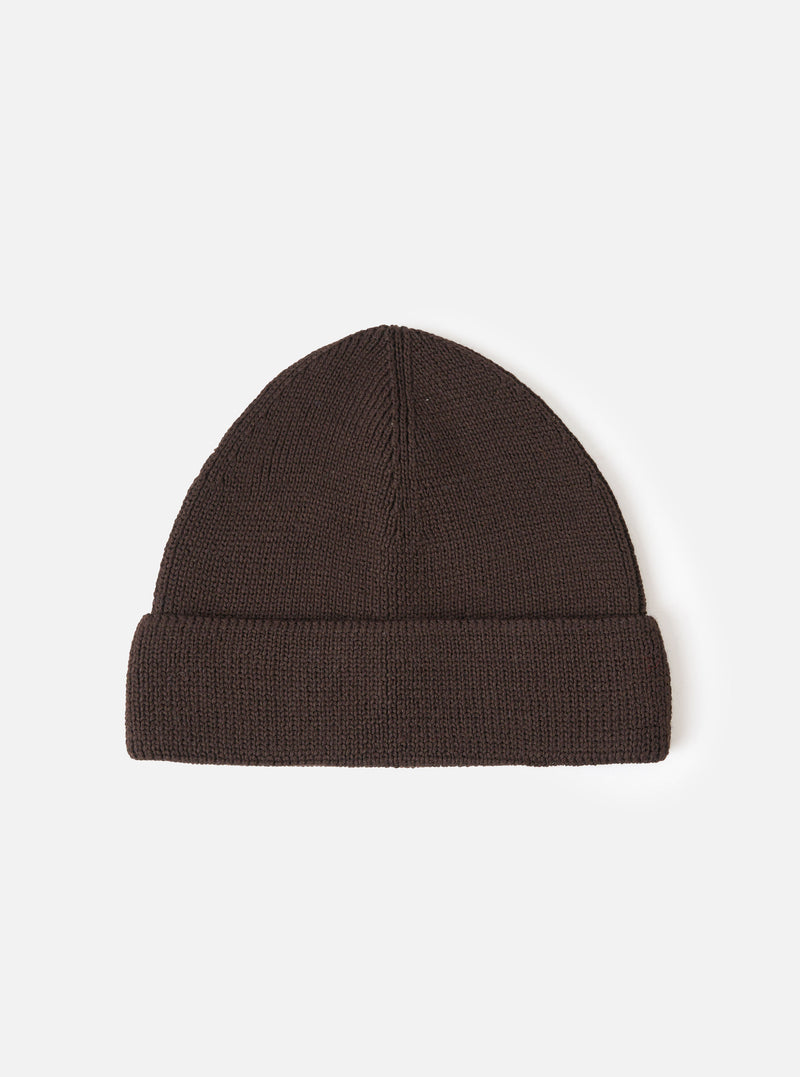 A Brown Merino Knit Watch Cap displayed flat against a plain studio background. The classic knitted beanie features a soft ribbed texture, a turn-up cuff, and a comfortable stretchy fit in rich brown merino wool.