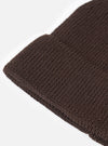 An angled view of the Brown Merino Knit Watch Cap on a plain neutral background, highlighting the full shape of the ribbed beanie, pinched crown construction, and rolled cuff detail in rich brown wool.