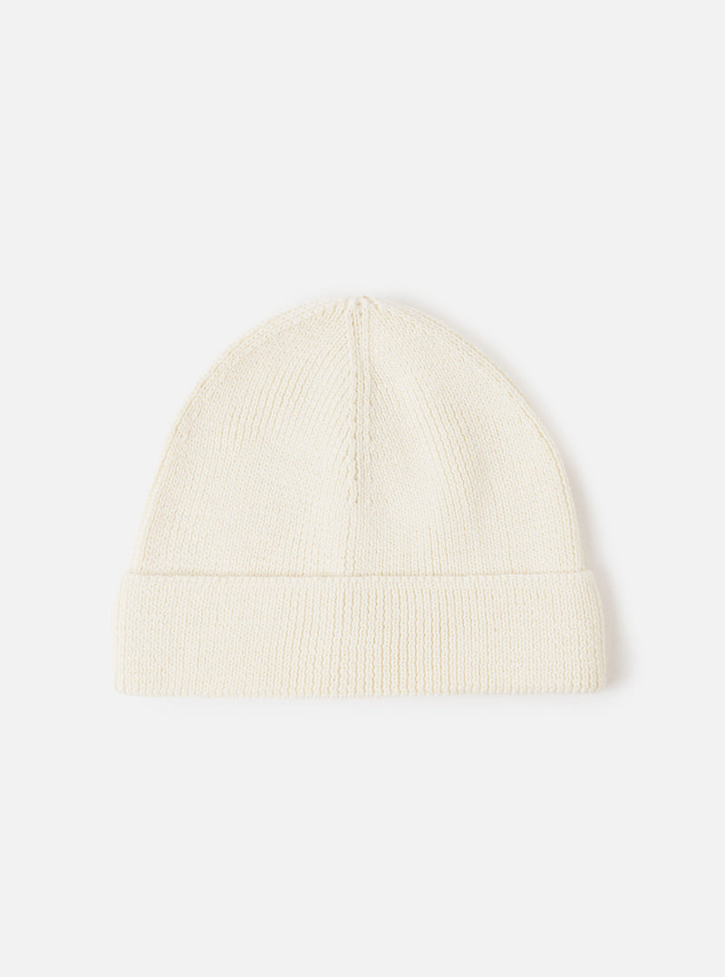 An Ecru Merino Knit Watch Cap displayed flat against a plain studio background. The classic knitted beanie features a soft ribbed texture, a turn-up cuff, and a comfortable stretchy fit in off-white ecru merino wool.