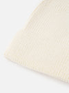 An angled view of the Ecru Merino Knit Watch Cap on a plain neutral background, highlighting the full shape of the ribbed beanie, pinched crown construction, and rolled cuff detail in off-white ecru wool.
