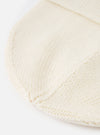 A detailed close-up shot of the Ecru Merino Knit Watch Cap against a plain white background. The image highlights the fine ribbed texture, folded cuff, and soft off-white wool construction of the hat.