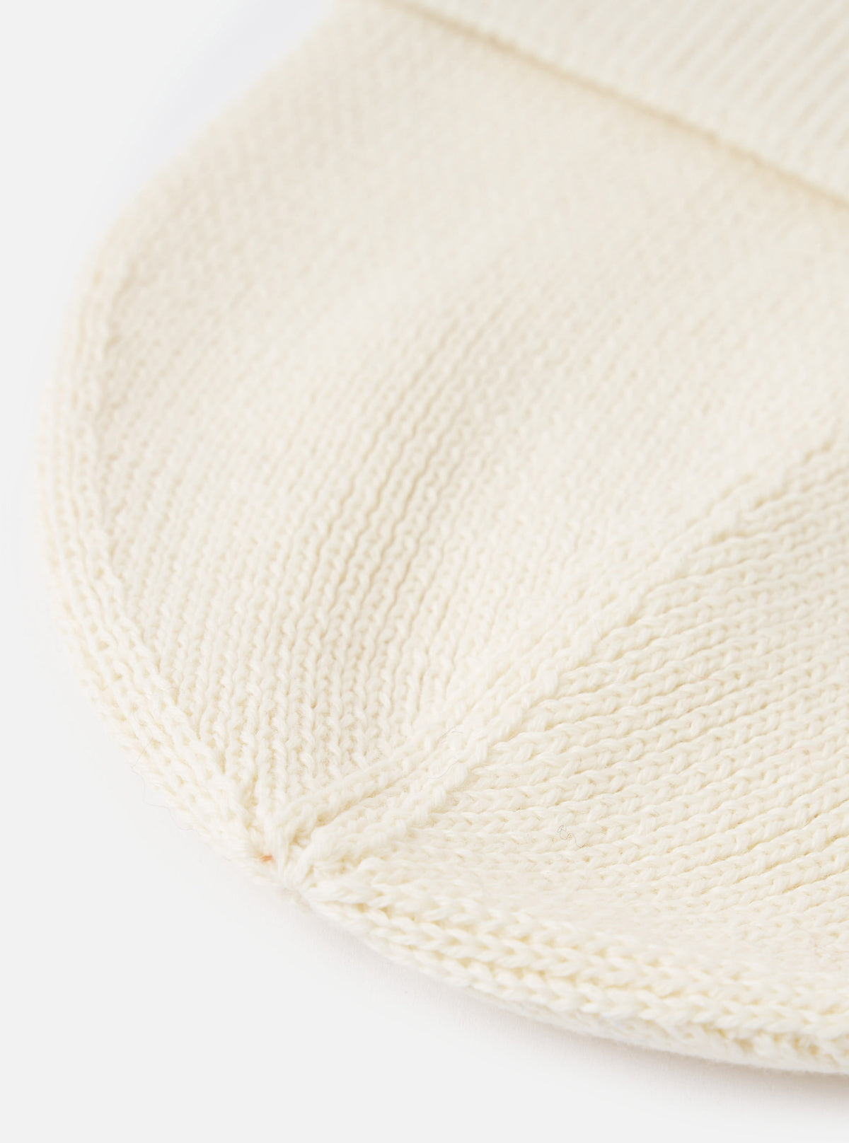 A detailed close-up shot of the Ecru Merino Knit Watch Cap against a plain white background. The image highlights the fine ribbed texture, folded cuff, and soft off-white wool construction of the hat.