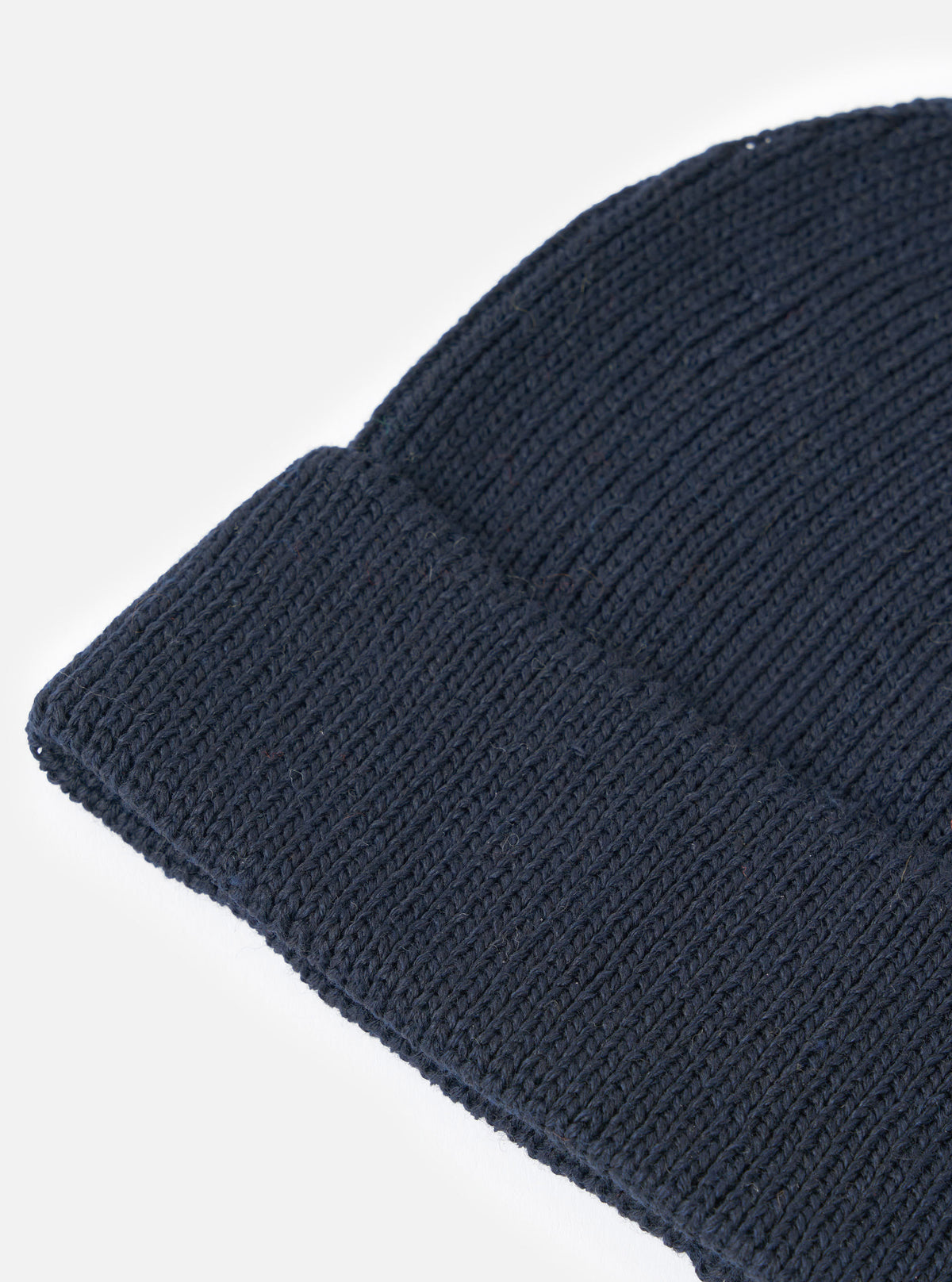 An angled product shot of the Navy Merino Knit Watch Cap set on a solid white background. The folded rim and textured ribbing of the dark blue wool blend knit are clearly displayed in focus.