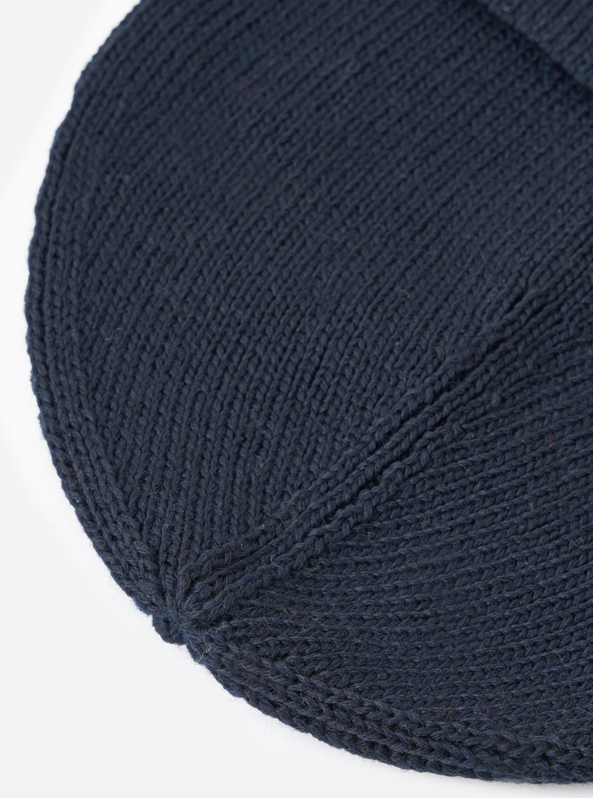 A close-up view focusing on the texture and crown of the Navy Merino Knit Watch Cap against a stark white background, showcasing the fine ribbed stitch work and soft navy merino wool yarn.