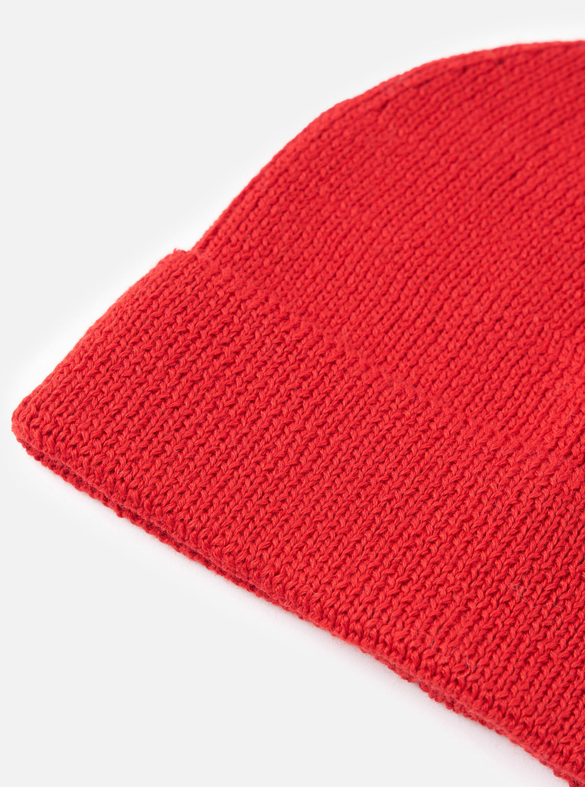 An angled view of the Red Merino Knit Watch Cap isolated on a white background. The description highlights the rich red merino wool fabric, clean stitched seams, and folded ribbed hem of the hat.