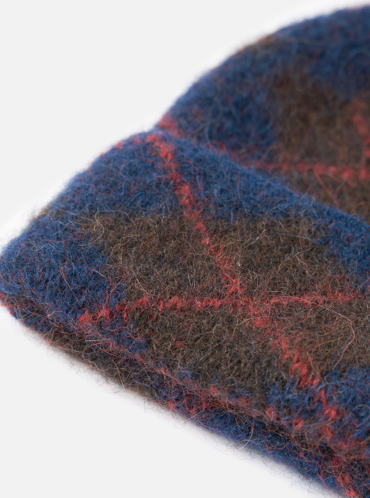 An angled view of the Navy Alpaca Argyle Argyll Hat shown against a stark white background. The shot displays the textured alpaca yarn construction, folded rim, and subtle diamond argyle pattern running along the body of the navy knit hat.