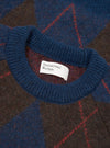 A close-up detail shot of the Navy Alpaca Argyle Lyon Crew against a plain white background. The image showcases the fuzzy texture of the alpaca wool blend yarn, ribbed crew collar, and intricate navy argyle knit pattern.