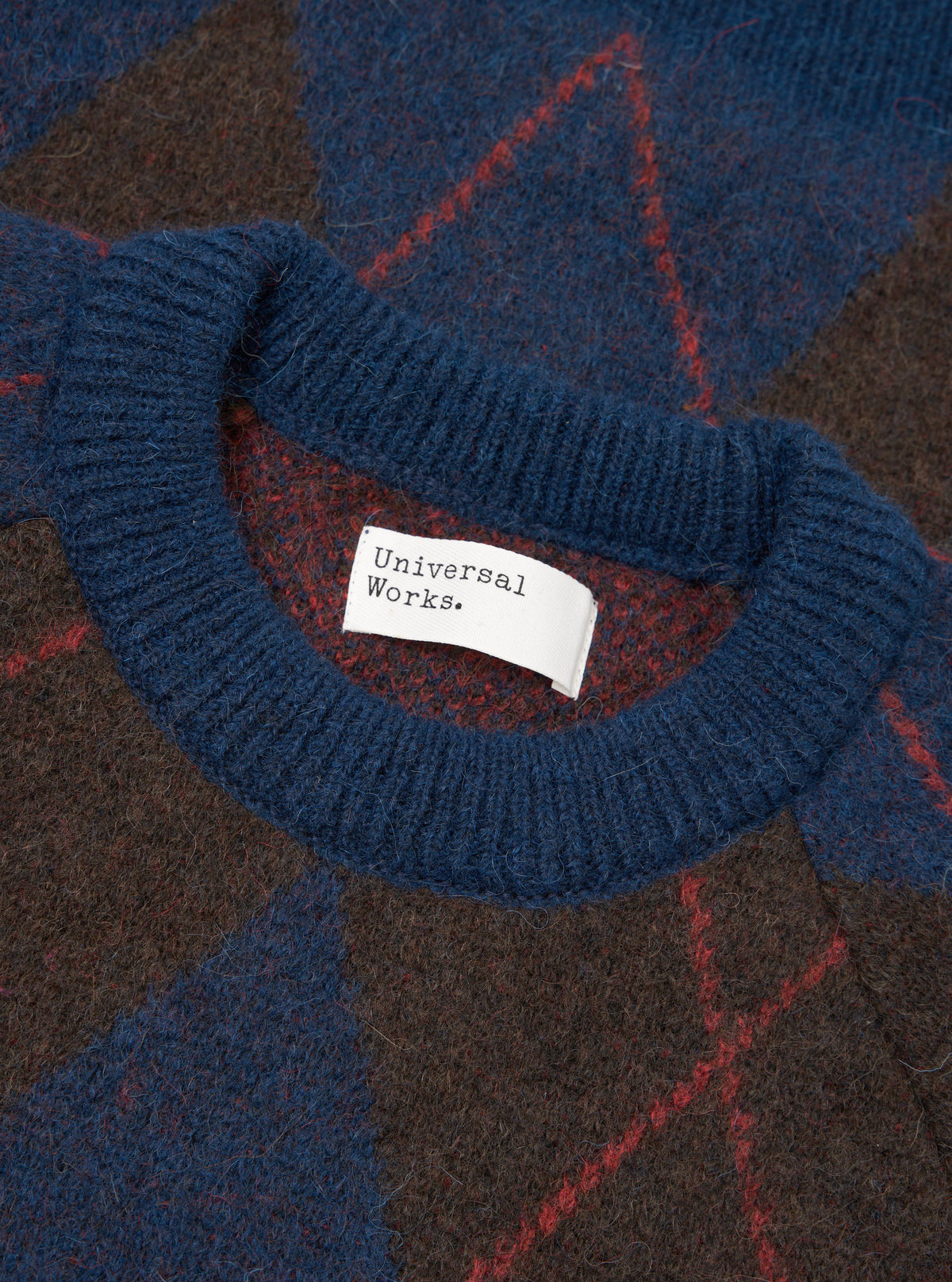 A close-up detail shot of the Navy Alpaca Argyle Lyon Crew against a plain white background. The image showcases the fuzzy texture of the alpaca wool blend yarn, ribbed crew collar, and intricate navy argyle knit pattern.