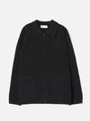Black ribbed-knit zip cardigan laid flat on a light grey seamless backdrop. Features a spread collar, full-length zip fastening, raglan sleeves, two large patch pockets at the hem, and a wide ribbed waistband. Universal Works woven label visible at the inner collar. No model or mannequin present.
