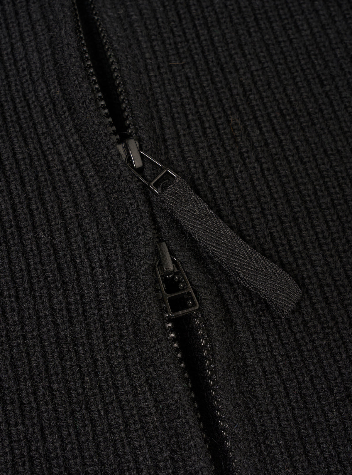 A close-up detail view of the Black Eco Wool Zip Cardigan set against a white background. The image focuses on the textured eco wool fabric, silver-tone zipper puller, high collar construction, and neatly finished zip track.