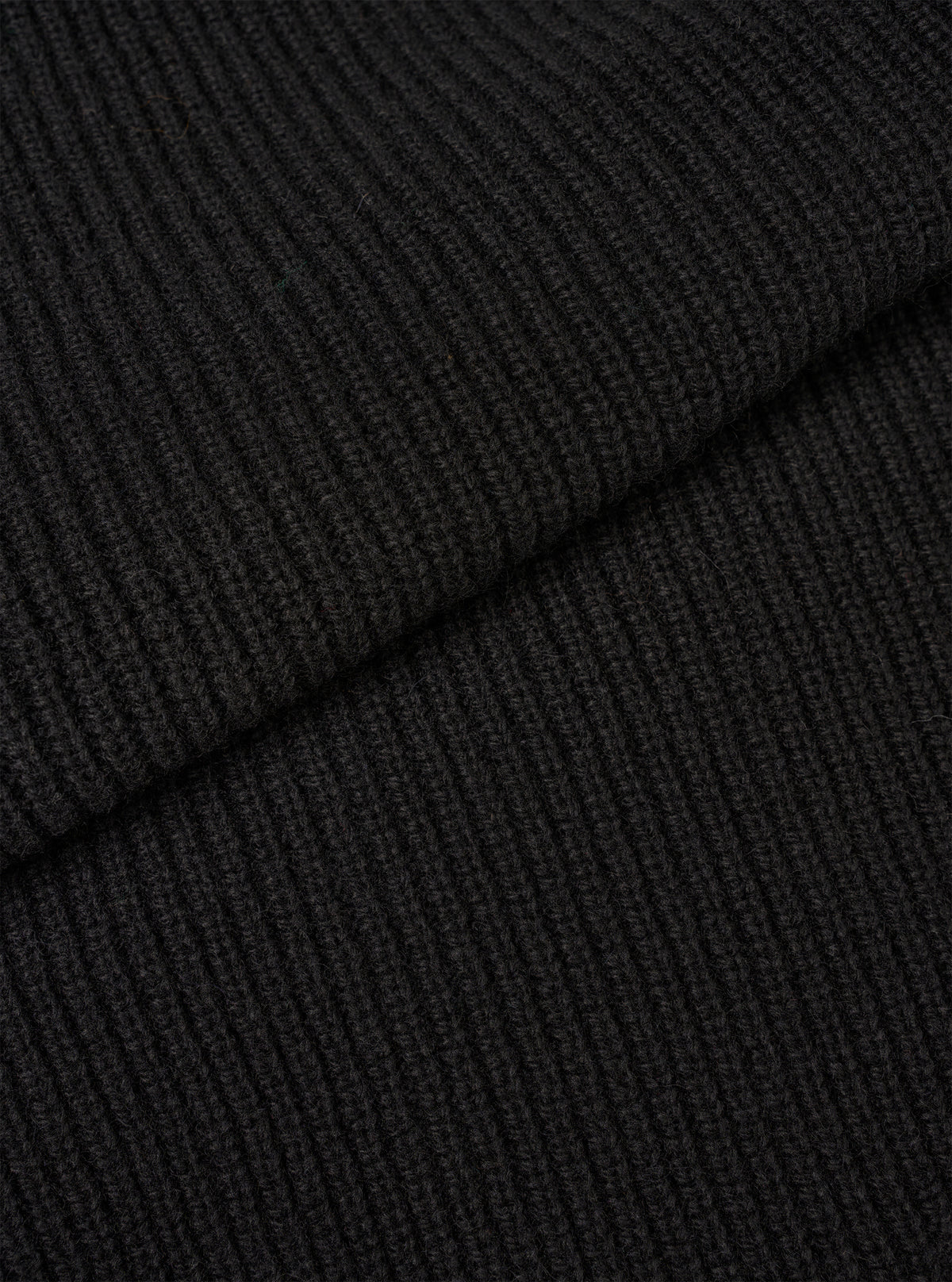 An extreme close-up fabric swatch shot showing the material of the Black Eco Wool Zip Cardigan. The photo details the dense, tactile texture of the black and dark grey eco wool yarn knitted together in a soft, premium weave.