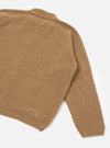 Close-up flat lay of a tawny eco wool zip cardigan on a white studio backdrop. The ribbed knit texture is visible across the body and raglan sleeve. A ribbed cuff and ribbed hem band are shown. A small zip pull is visible at the bottom hem. The spread collar is partially visible at the top.