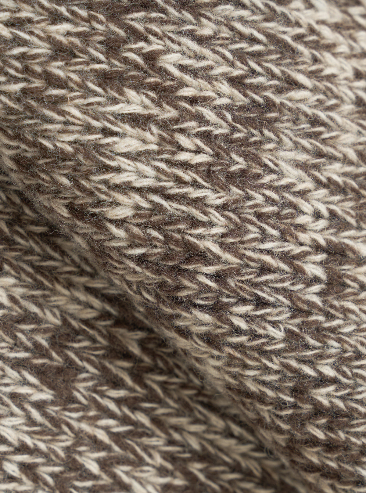An extreme close-up fabric swatch shot of the Ecru/Brown Lambswool Zip Cardigan. The photo details the thick, warm texture of pure lambswool yarn, showcasing blended ecru and brown fibers knitted together into a soft fabric.