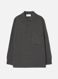 Charcoal merino knit pullover shirt laid flat on a light grey seamless backdrop. Features a wide point collar, four-button placket with dark buttons, a left chest patch pocket, long sleeves with ribbed cuffs, and a ribbed hem. Fine smooth knit texture throughout. Universal Works woven label at back neck.