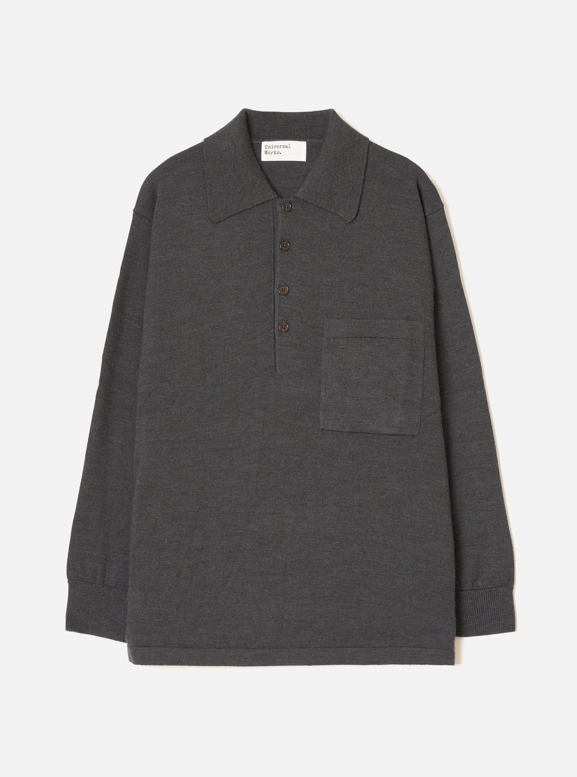 Charcoal merino knit pullover shirt laid flat on a light grey seamless backdrop. Features a wide point collar, four-button placket with dark buttons, a left chest patch pocket, long sleeves with ribbed cuffs, and a ribbed hem. Fine smooth knit texture throughout. Universal Works woven label at back neck.