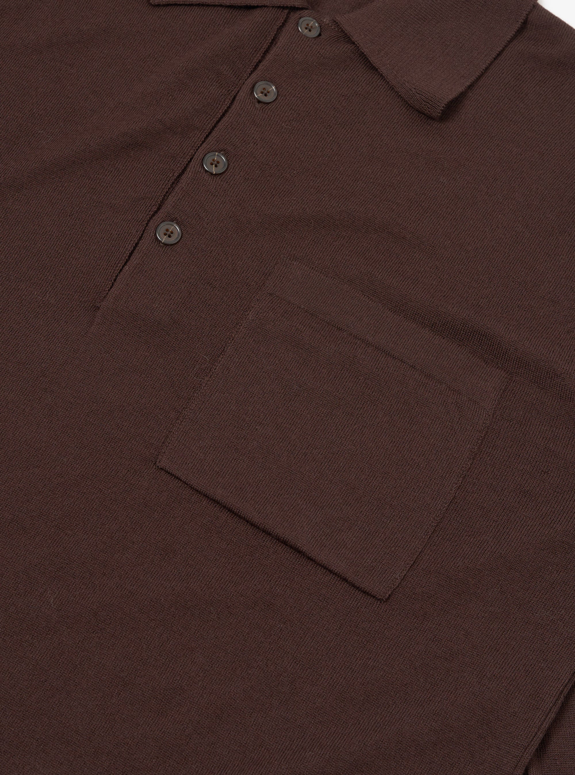 Close-up flat lay of an espresso brown merino knit polo shirt on a plain white surface. The ribbed knit collar, three-button placket with dark four-hole buttons, and a chest patch pocket are clearly visible. The fine knit texture is evident across the body.