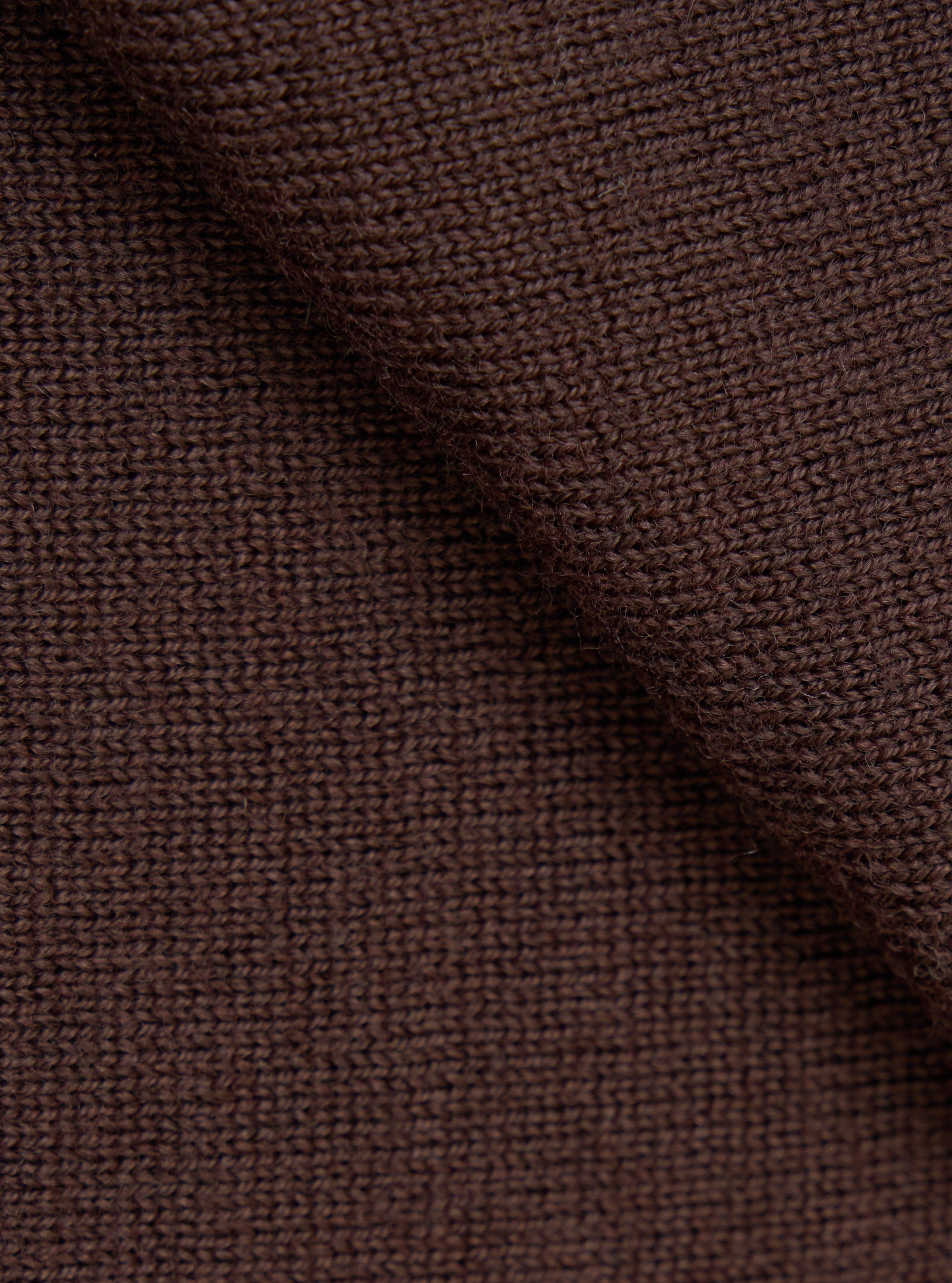 Close-up detail shot of the espresso brown merino knit fabric, showing a uniform stocking stitch construction with a slightly heathered texture. The fabric is gathered and folded to highlight the knit structure and drape. No background is visible.