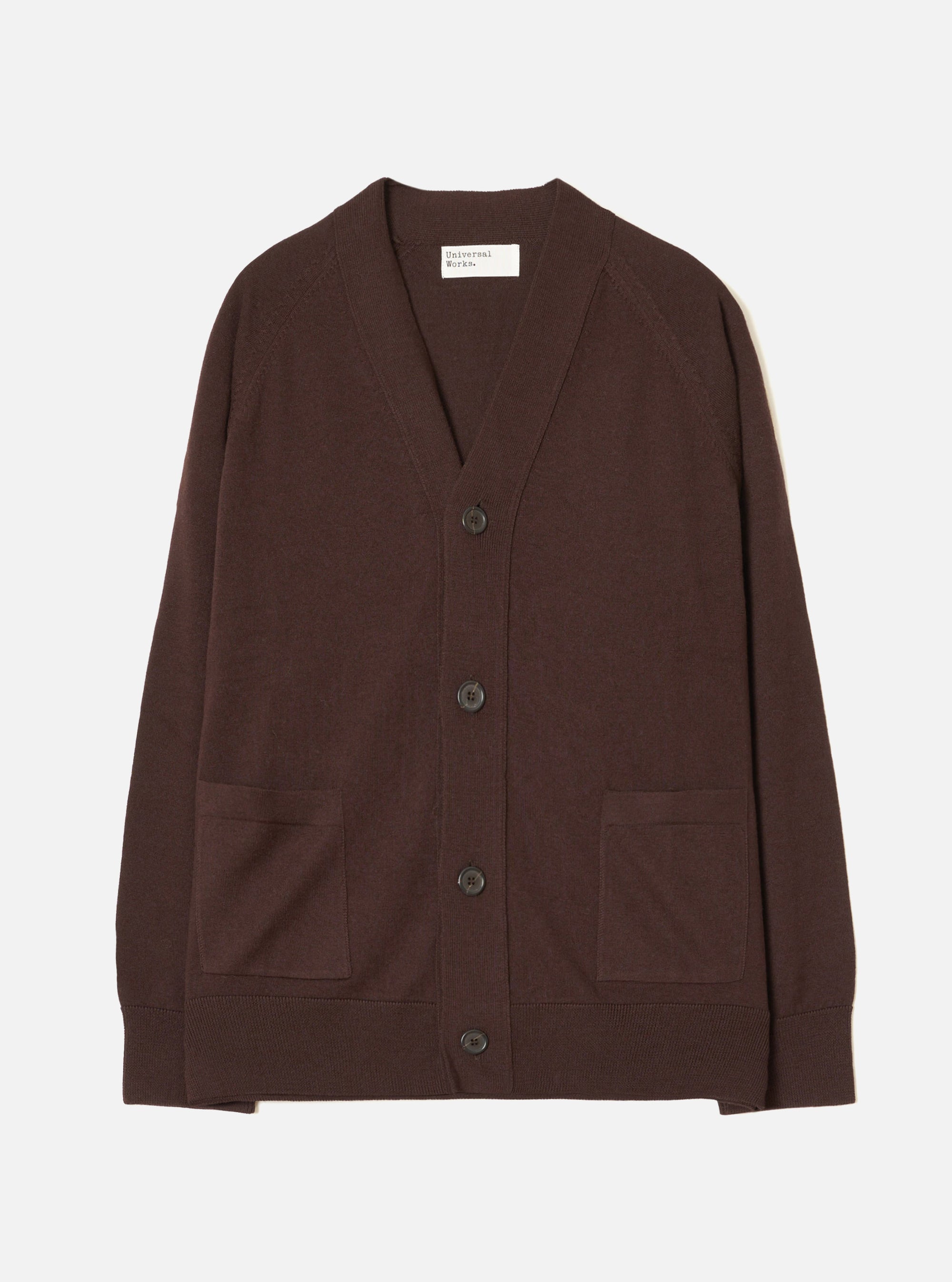 Espresso brown merino knit cardigan laid flat on a light grey backdrop. V-neck with a ribbed placket, four dark horn-effect buttons, two patch pockets at the hip, raglan sleeves, ribbed cuffs and hem. Universal Works woven label visible at the inner neckline.