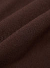 Close-up detail shot of the espresso brown merino knit fabric, showing the fine, even knit structure and a raised ribbed trim running diagonally across the frame. The dense, smooth texture and yarn quality are clearly visible against the draped folds of the garment.