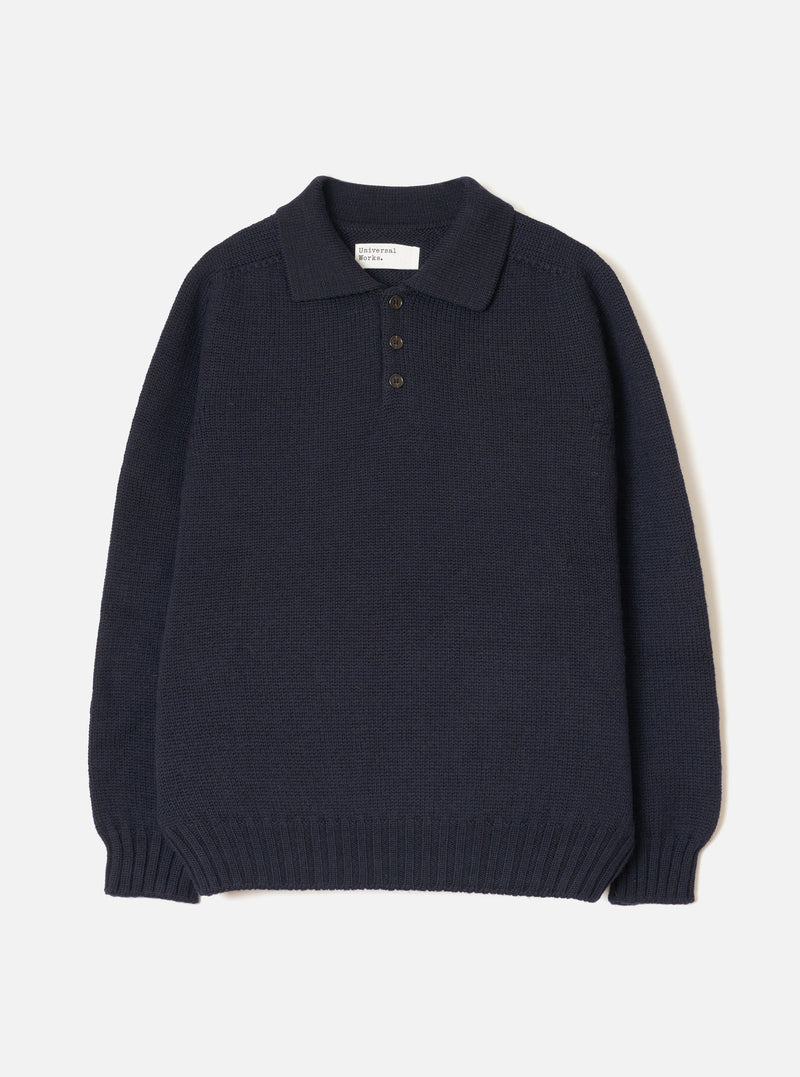 The Navy Shetland Wild Curtis Sweater is laid flat on a light grey seamless backdrop. Designed as a polo knit, it features a spread collar, a three-button front placket, a chunky wool knit body, long sleeves, and wide ribbed hem and cuffs.