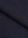 Close-up detail shot of the navy Shetland Wild Curtis sweater fabric. The chunky knit texture is shown in high detail, revealing a moss or seed stitch construction with a ribbed section visible at the top. The wool yarn is a deep navy, shot against no background.
