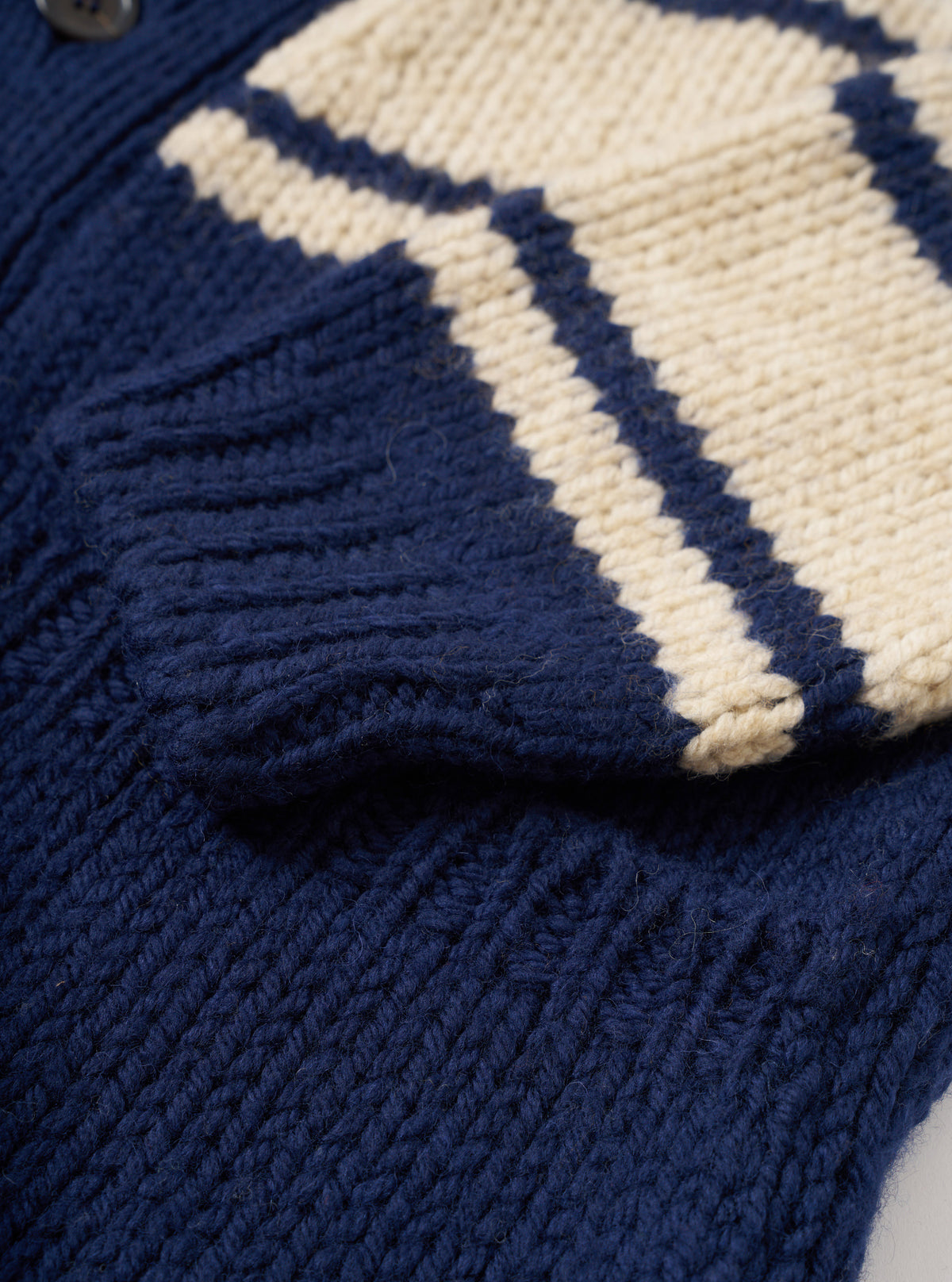 Close-up detail shot of the Navy Chunky Knit Stripe Langdale Cardigan on a plain white background. Focuses on the dark buttons, V-neckline, ribbed trim, front pocket, and textured navy and contrasting intarsia stripe wool knit.