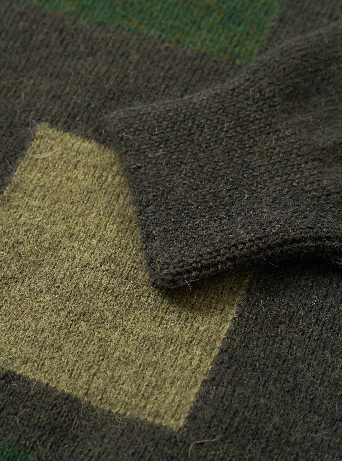 Close-up detail view of the Olive British Wool Lyon Crew sweater against a stark white studio background. Focuses on the ribbed crew collar, raglan sleeve construction, and fine texture of the olive green British wool yarn.