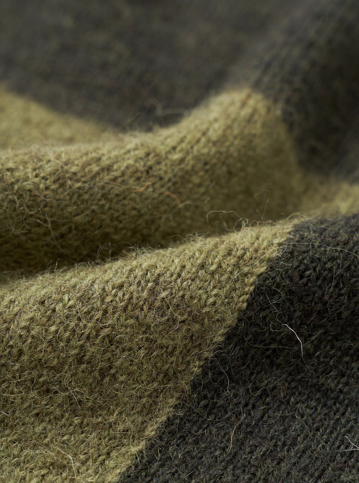 A close-up fabric swatch of the Olive British Wool Lyon Crew sweater. The detailed shot emphasizes the rich marled pattern, soft depth, and heavy weave of the olive green British wool material against a clean white background.