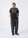 A male model standing against a plain studio background wearing the Grey Liverpool Check Oxford Pant paired with casual footwear, demonstrating the relaxed loose fit, wide leg silhouette, and drape of the grey check trousers.