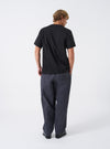 A model wearing the Grey Liverpool Check Oxford Pant, shown from the side against a neutral white backdrop. The photo highlights the comfortable fit, pleated waistband, side pockets, and full length drape of the checked trousers.
