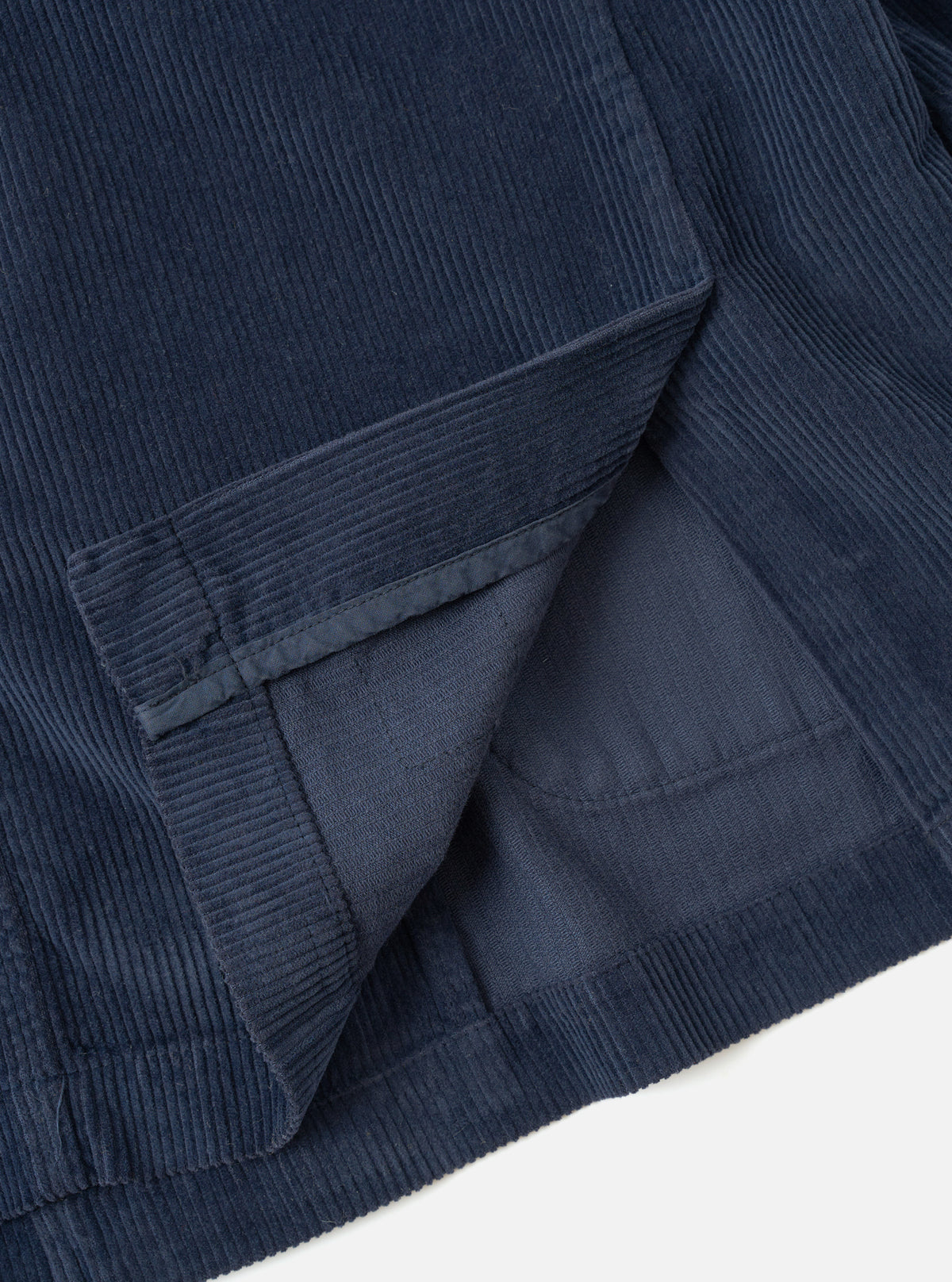 An angled detail view of the Dark Navy Cord Manor Jacket against a bright white studio background, highlighting the rich fine-wale corduroy fabric, lapel construction, dark buttons, and front pocket design.