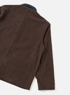 Rear and sleeve detail of a cacao brown corduroy utility jacket, shot flat on a light grey seamless backdrop. Wide-wale corduroy texture is prominent across the back panel and sleeve. A contrast navy corduroy collar is visible at the top. Diagonal back seams and a plain, unfinished hem are visible.