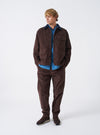 A male model wears the Cacao Cord Utility Jacket in a front-facing posture against a plain light studio background. The brown corduroy jacket features multiple utility front pockets and a neat collar.